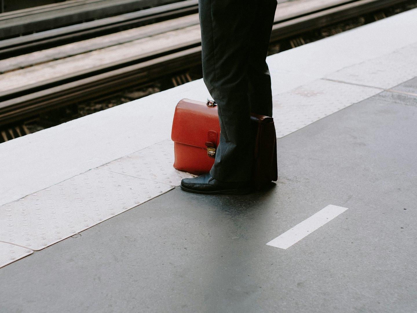 Un professionnel se tient sur le quai d'une gare avec une mallette.